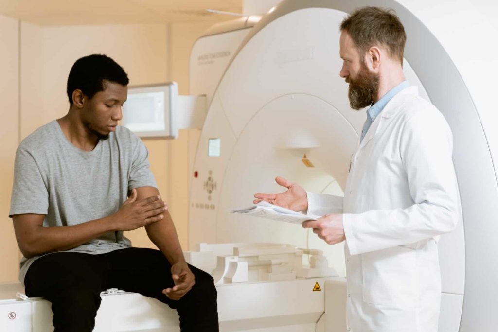 patient in a gray shirt sitting down and talking to a doctor by a body scanner