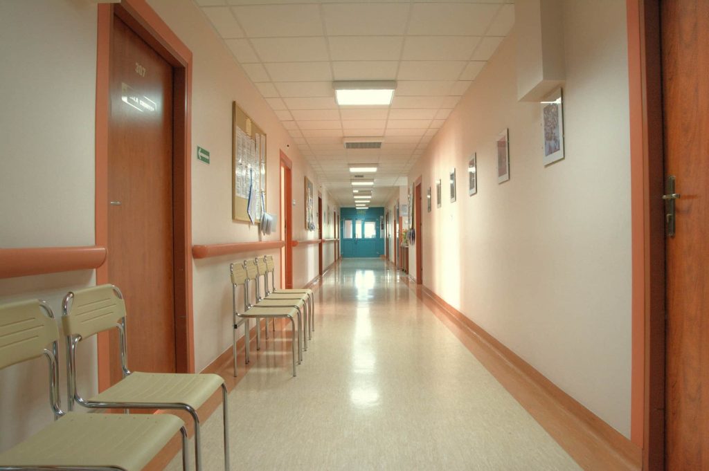 ALT TEXT (WITH IMAGE SOURCE): a hospital corridor with beige chairs and brown doors