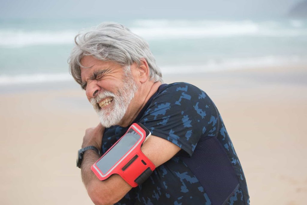 A man holding his shoulder in pain on the beach.