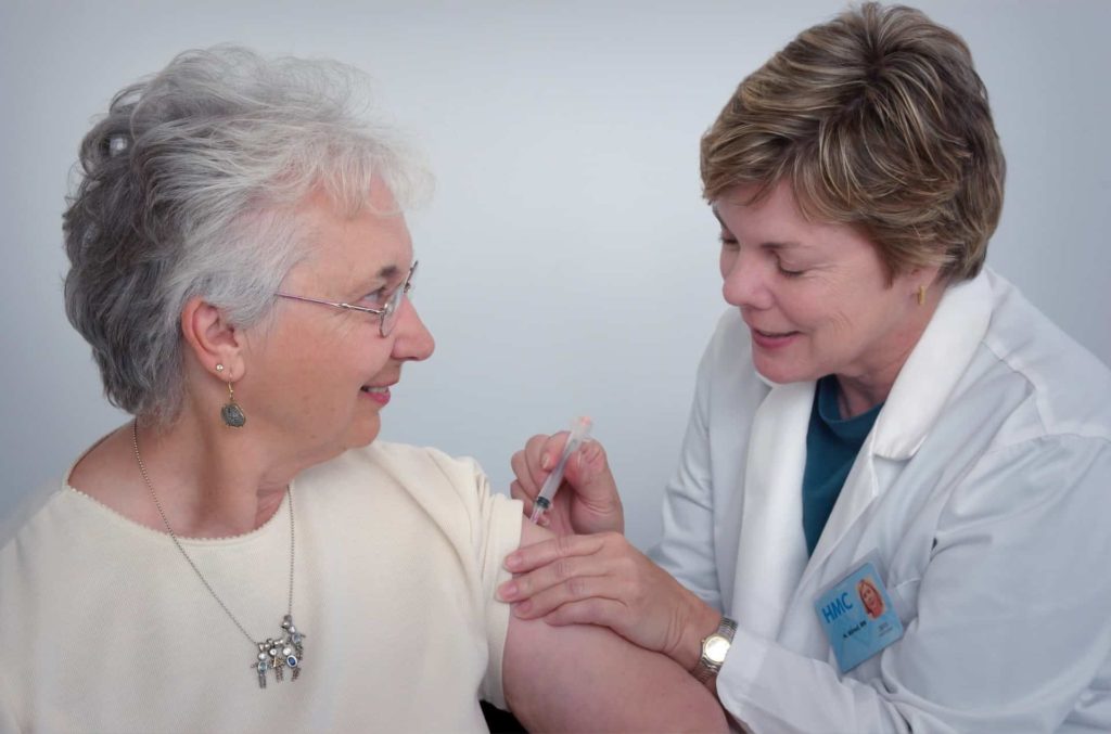 A medical provider giving an older woman a shot.