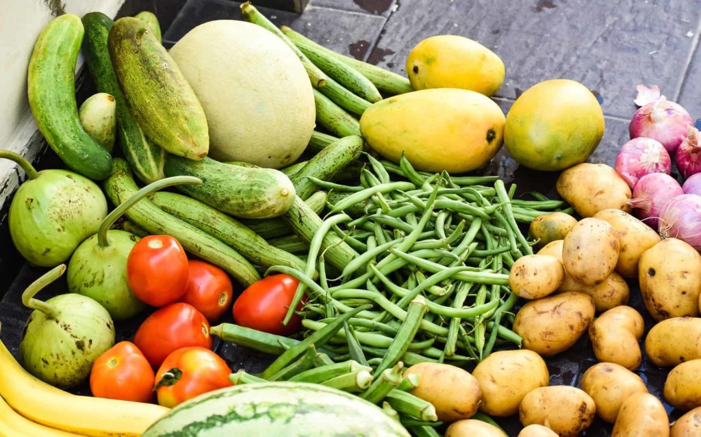 a pile of fresh fruits and vegetables such as green beans, bananas, and potatoes