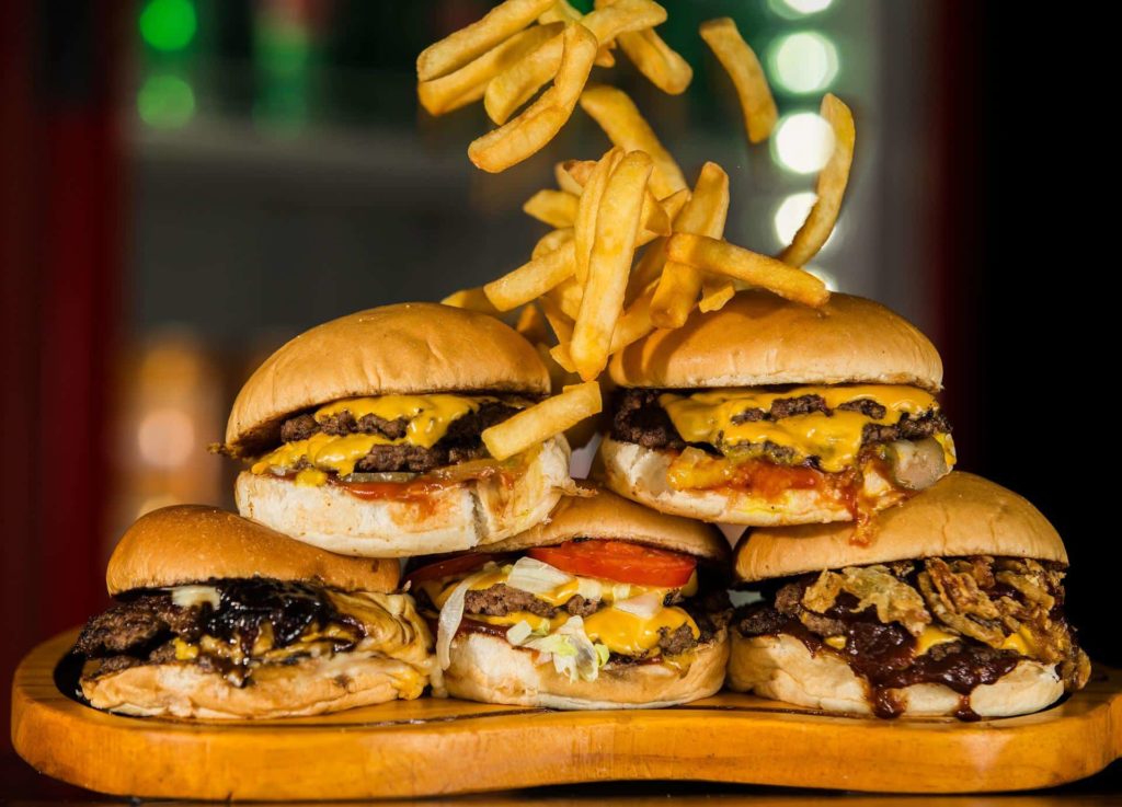 a wooden platter with several cheeseburgers stacked on top of each other with french fries
